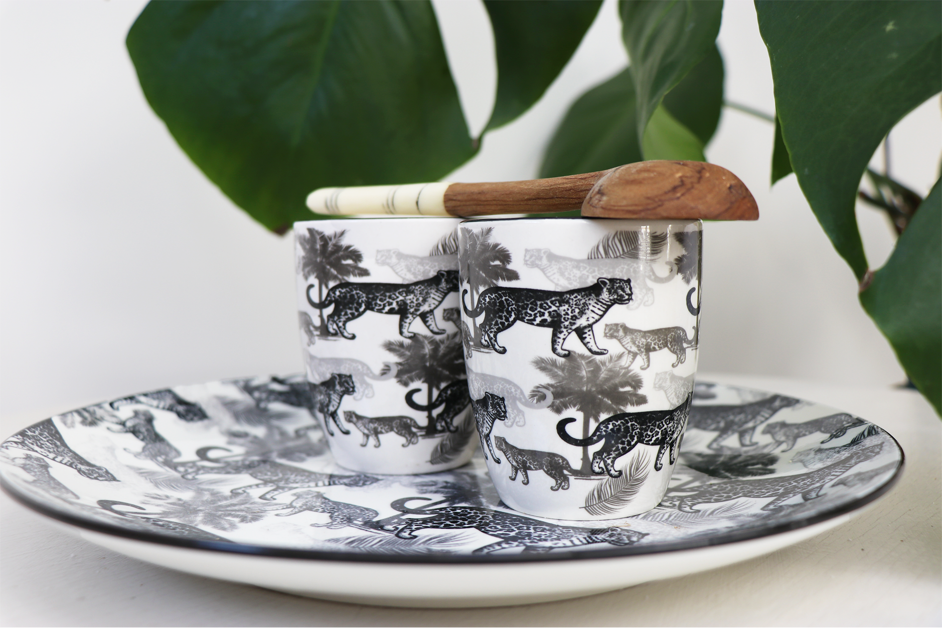 Deux tasses à motifs de guépards sur une assiette assortie, avec une cuillère en bois sur le dessus.