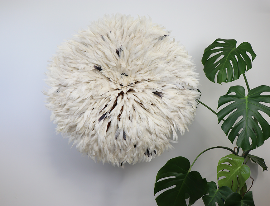 Décoration murale blanche Juju Hat avec plumes à côté d'une plante verte à grandes feuilles dans un intérieur moderne.