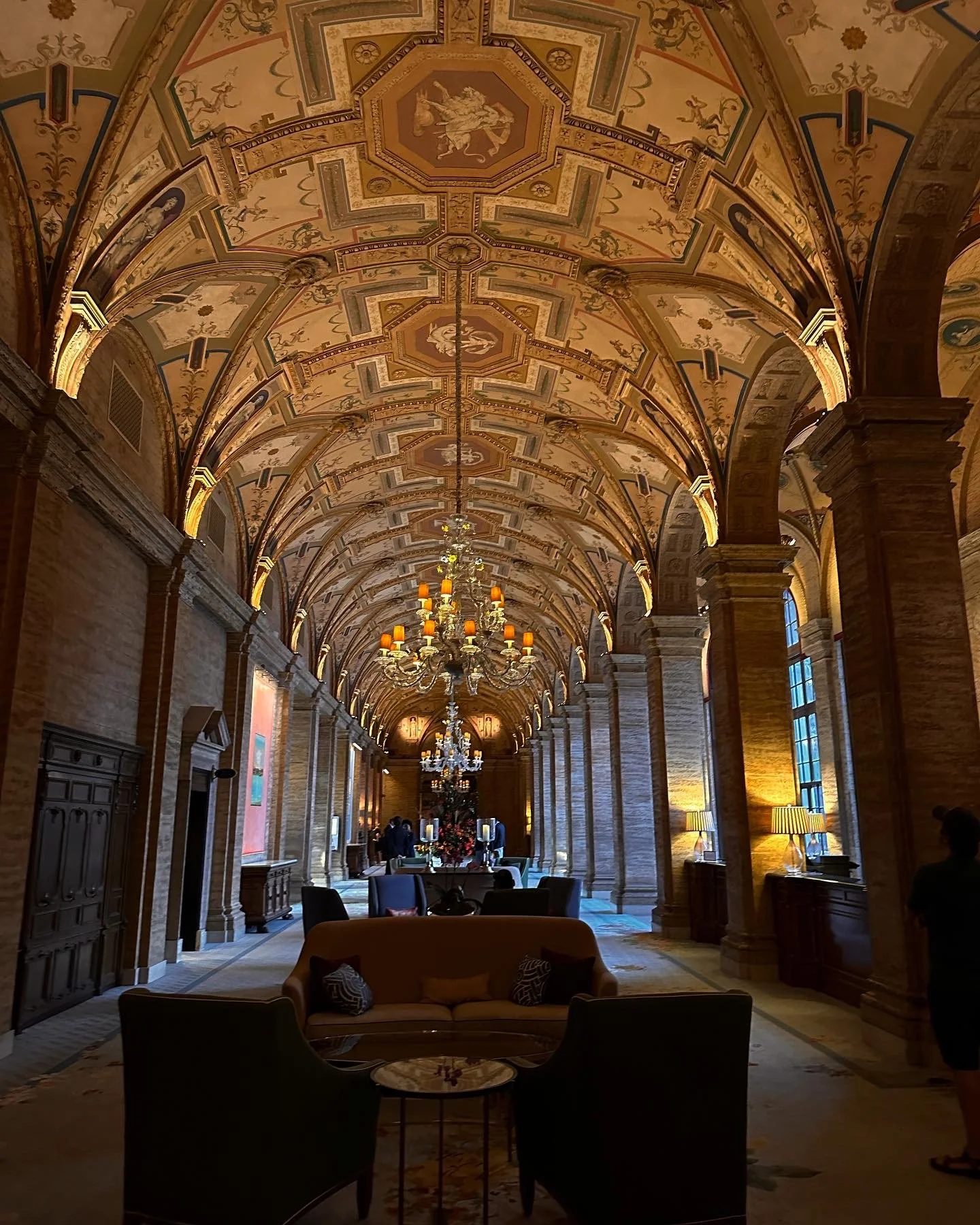 Luxurious hotel lobby with ornate painted ceilings, chandeliers, large windows, and plush seating area.