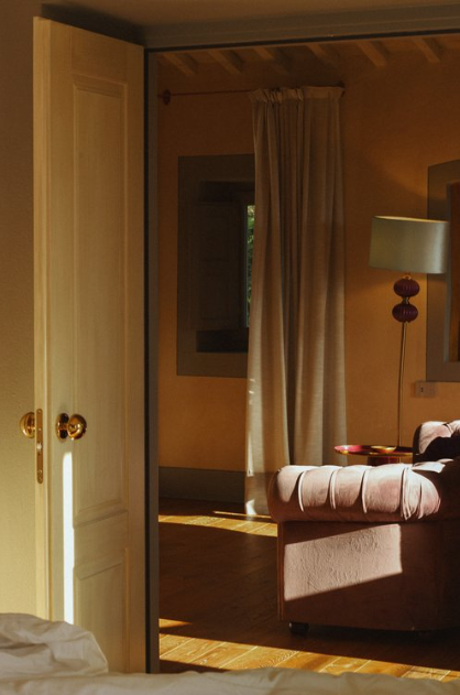 Part of a cozy living room with a pink armchair, a side table, and a lamp, partially seen through an open closet door with sunlight streaming in.