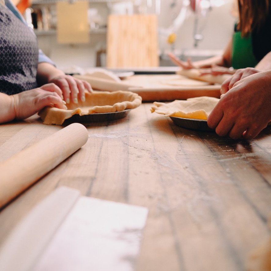People preparing pie crusts in a kitchen with rolling pins and dough.
