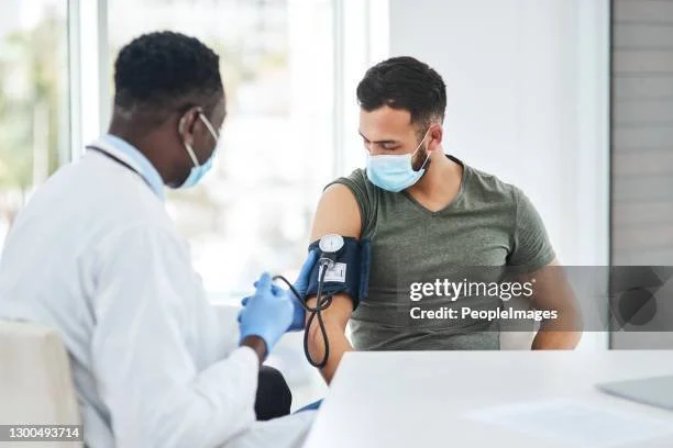 A healthcare professional administers an injection to a patient who is sitting in a medical office, both wearing masks.