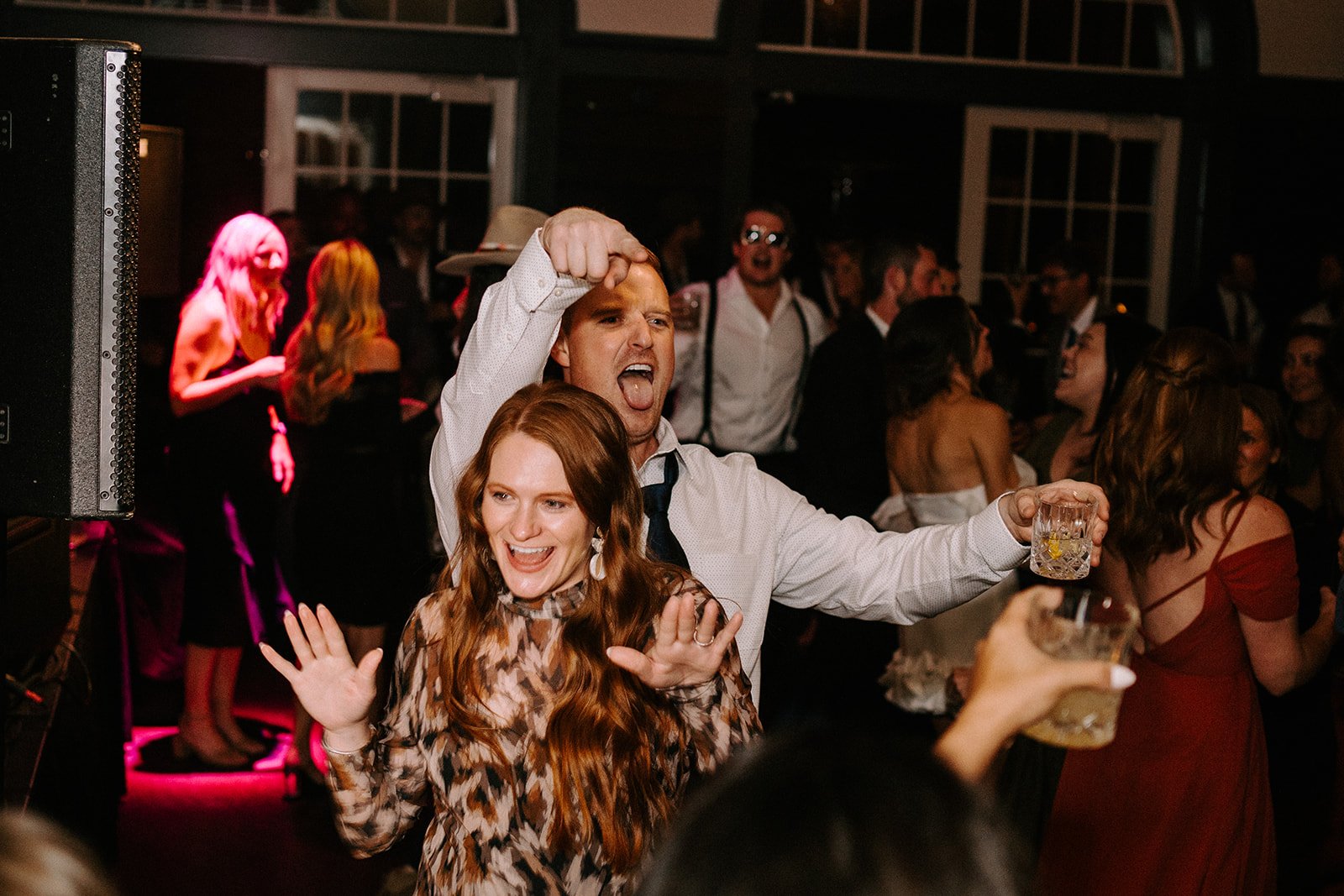 People dancing and celebrating at a party with drinks, colorful lighting, and a lively atmosphere.