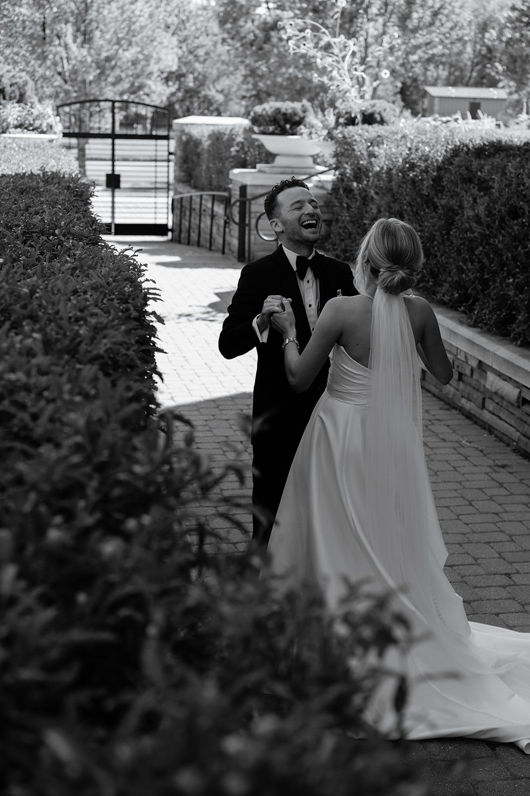Bride and groom smiling and holding hands in an outdoor garden setting.