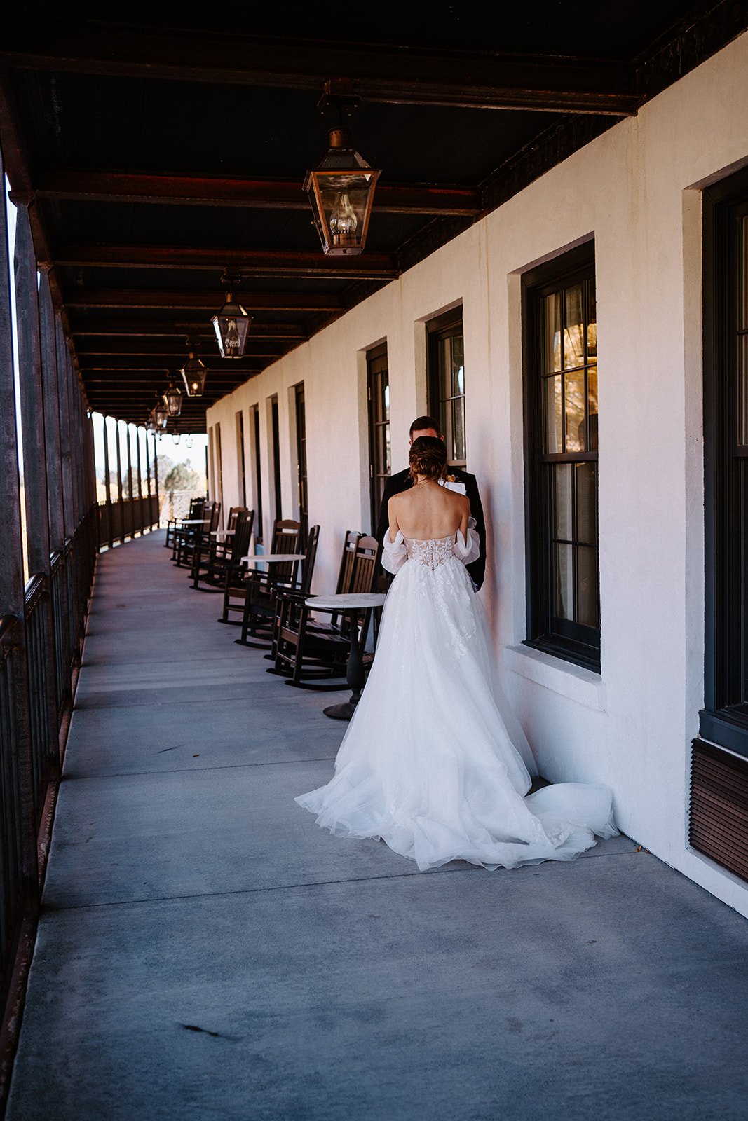 Bride in wedding dress standing on a porch with rocking chairs