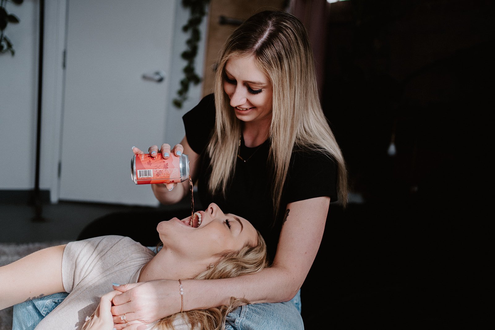Two women, one pouring drink into other's mouth from can.