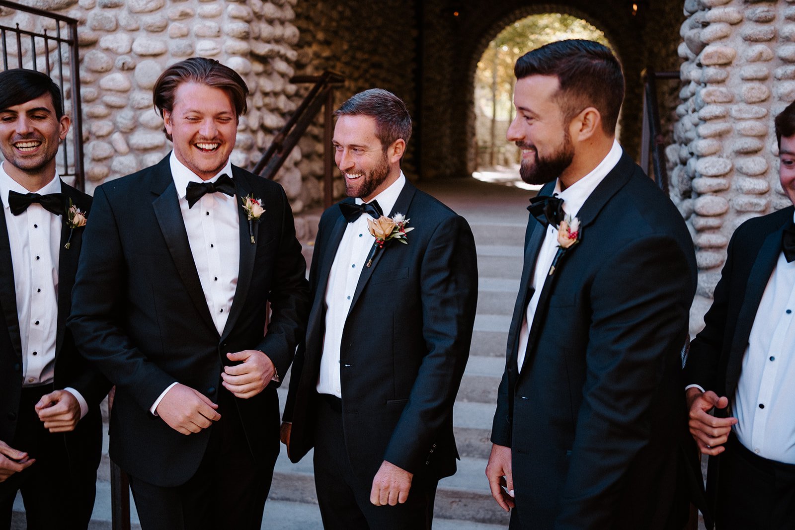 Group of men in tuxedos laughing at a wedding gathering.