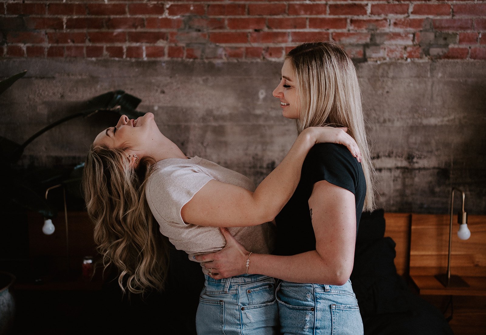 Two women embracing and laughing in front of a brick wall.