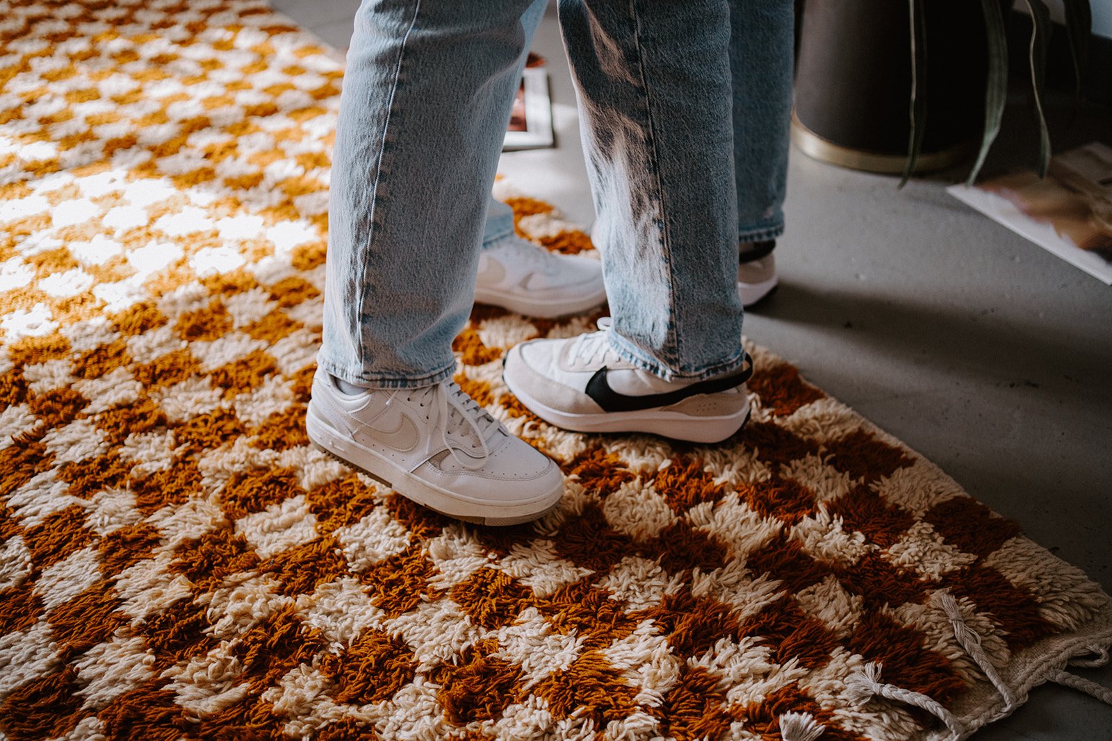 Two people wearing jeans and sneakers stand on a checkered rug.