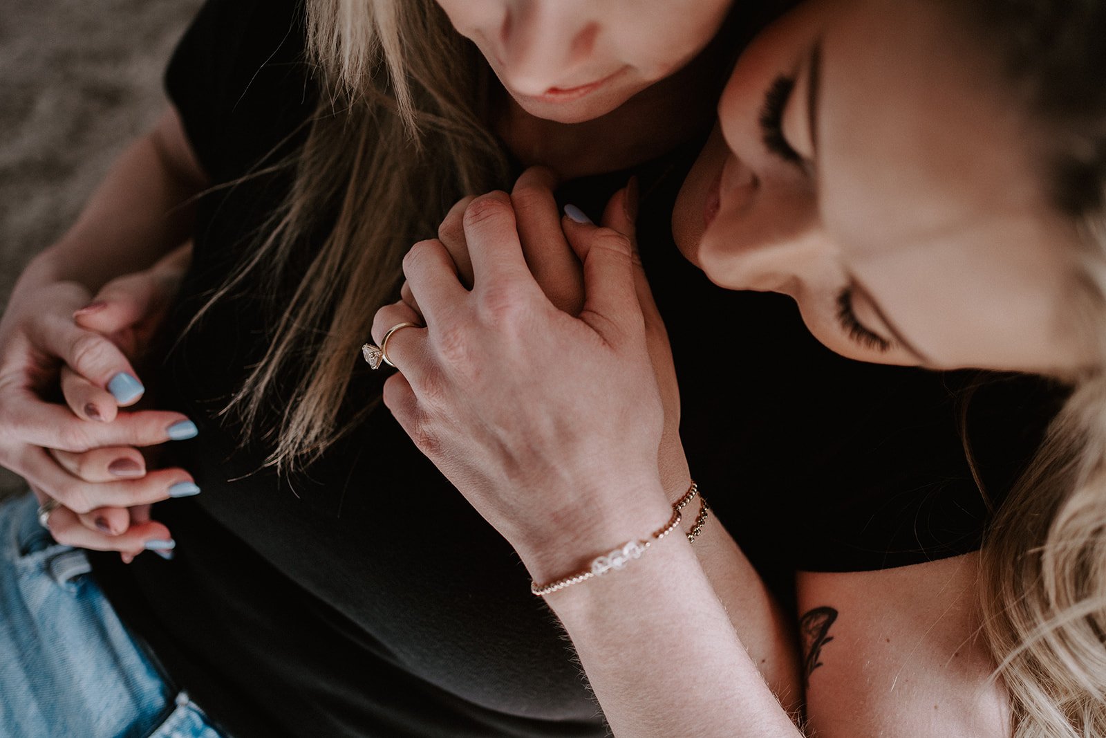 Close-up of two women holding hands, showing a diamond ring and bracelet on one woman's hand.