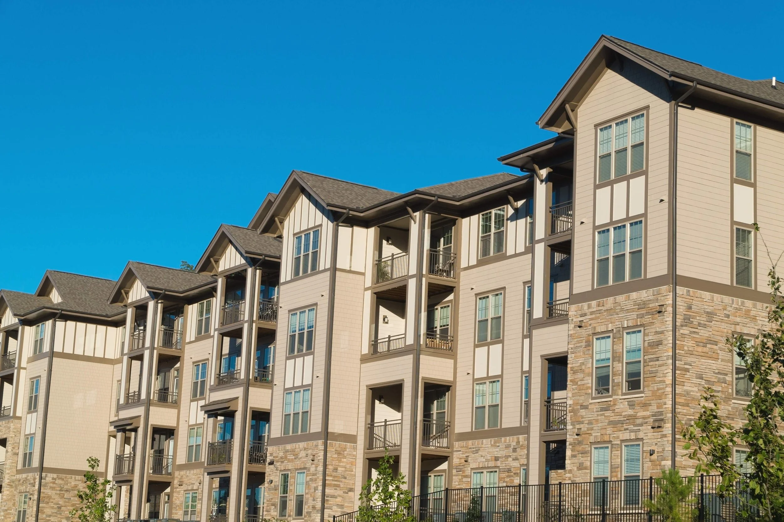 Multi-story apartment building with stone and siding exterior, peaked rooflines, and covered balconies.