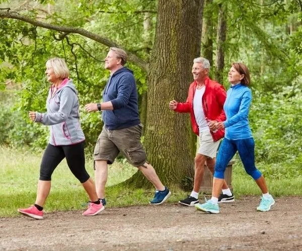 Quattro persone camminano in un parco verde, vestite con abbigliamento sportivo.