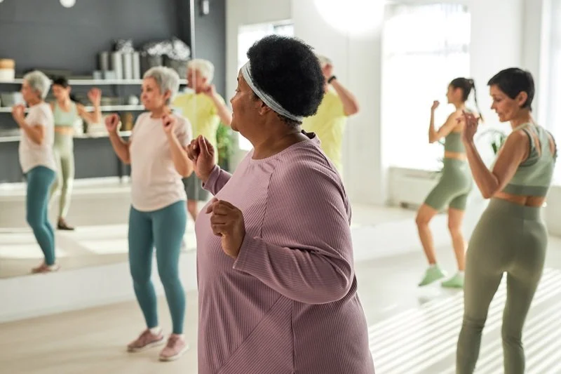 A small group of women moving together in a relaxed, non-performative way. Comfortable clothing. Different body types. Focus, not strain.