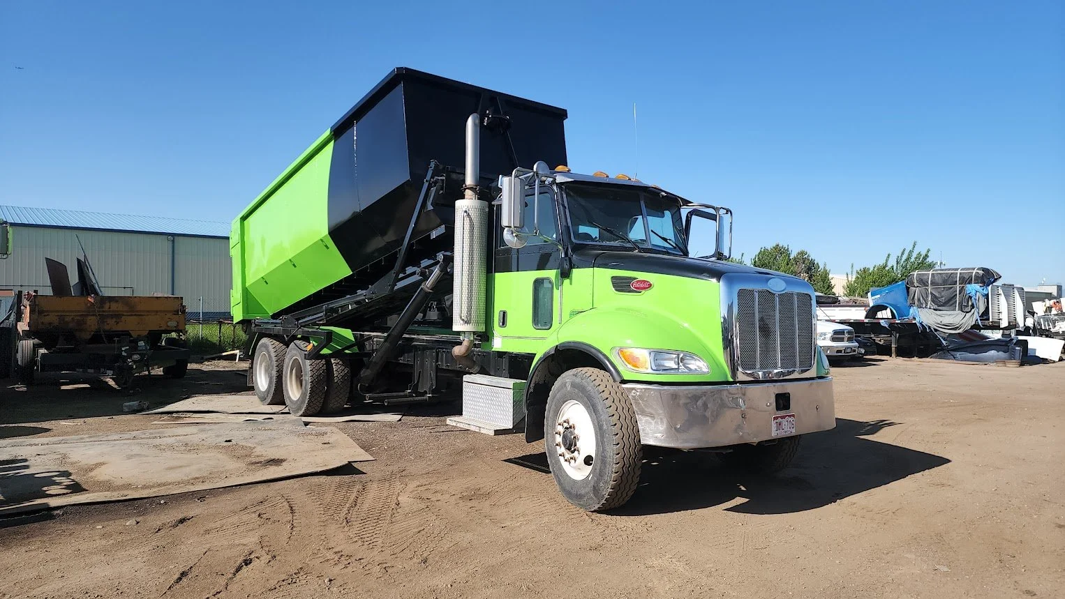 A green and black dump truck parked in a junkyard on a sunny day.