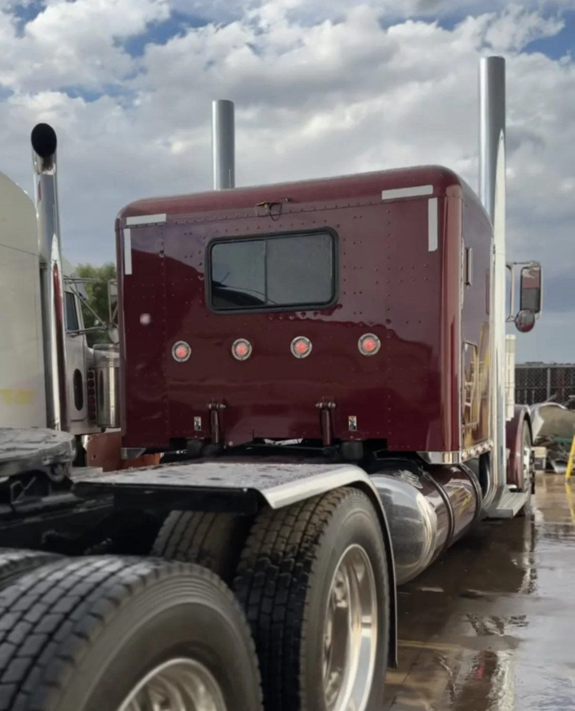 Red semi-truck tractor cab parked outdoors on wet ground with cloudy sky.