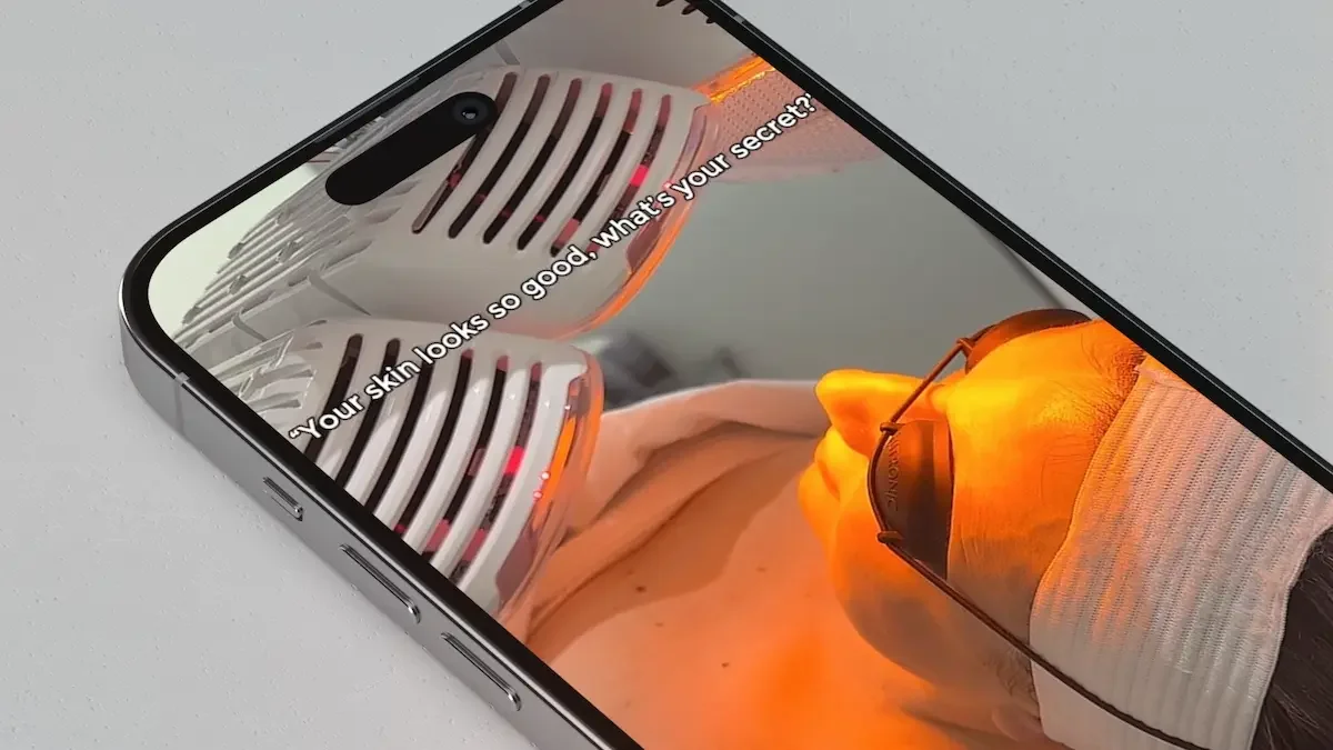 Smartphone displaying a digital marketing skincare advertisement for a medical spa with the client wearing goggles under a red LED light. The form of advertisement is an Instagram reel.