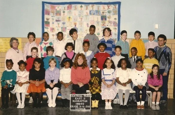 Group photo of elementary school students and teacher in classroom, with a bulletin board in the background, taken at Central Park East II School in Manhattan during the 1988-89 school year.