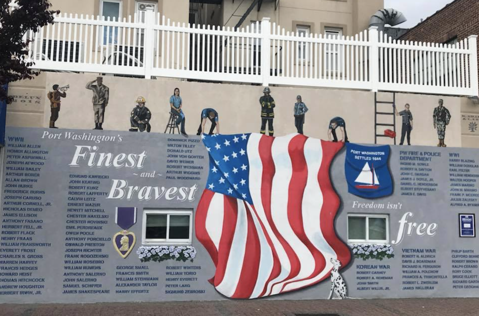 A mural honoring war veterans, featuring a large American flag in the center, with various figures representing different professions and war veterans painted along the top. The mural includes lists of names and the phrase "Finest and Bravest" and "F