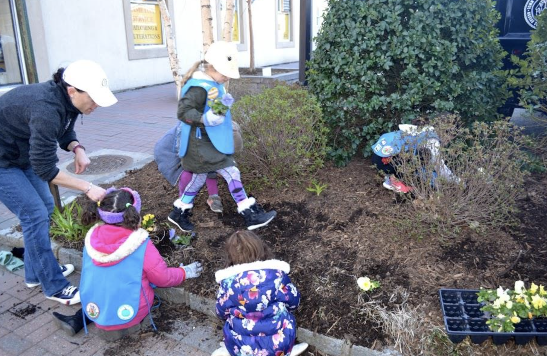 Adults and children planting flowers in a public garden bed.