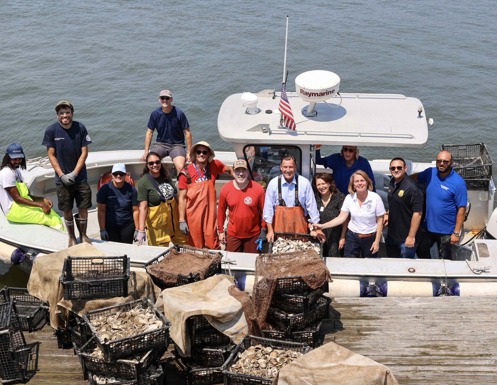 Group of people on a boat with crates of oyster shells on a dock