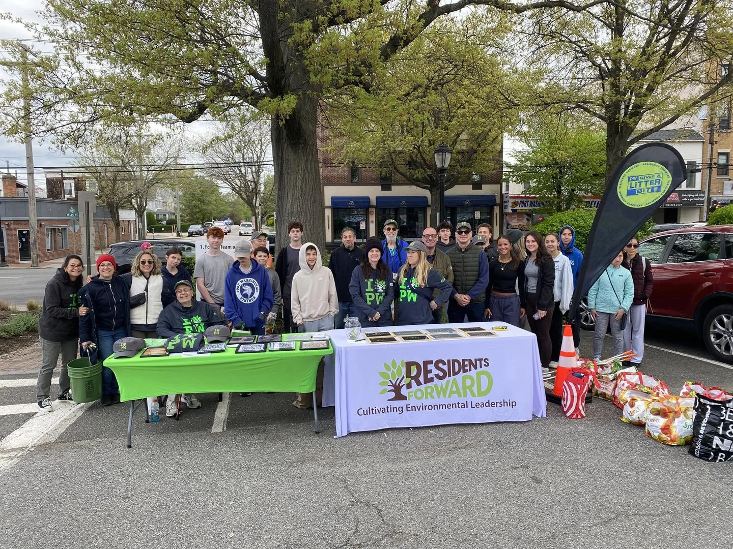 Group of people standing behind tables with environmental awareness materials in an outdoor setting, promoting residents' environmental leadership and litter pickup event.