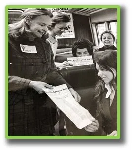 Group of women at a recognition event, with one woman handing a certificate to another, two others watching and smiling.