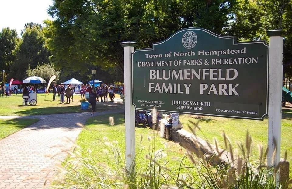 People enjoying a day at Blumenfeld Family Park in North Hempstead with tents and trees.