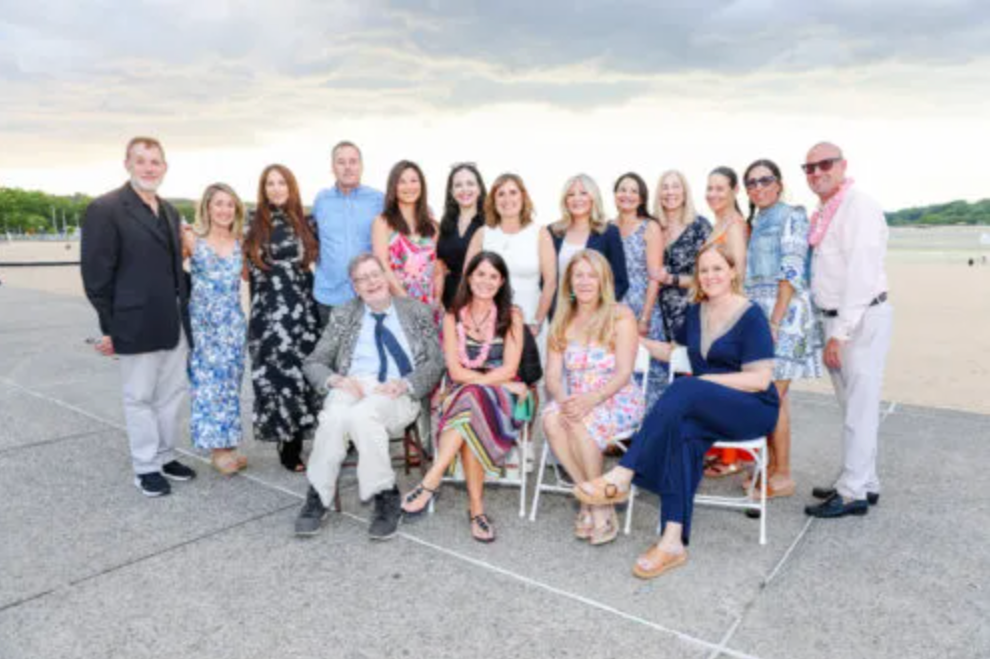 Group of diverse adults posing outdoors on a cloudy day, some sitting and some standing, dressed in colorful summer attire. Photo taken at the Residents Forward annual gala.
