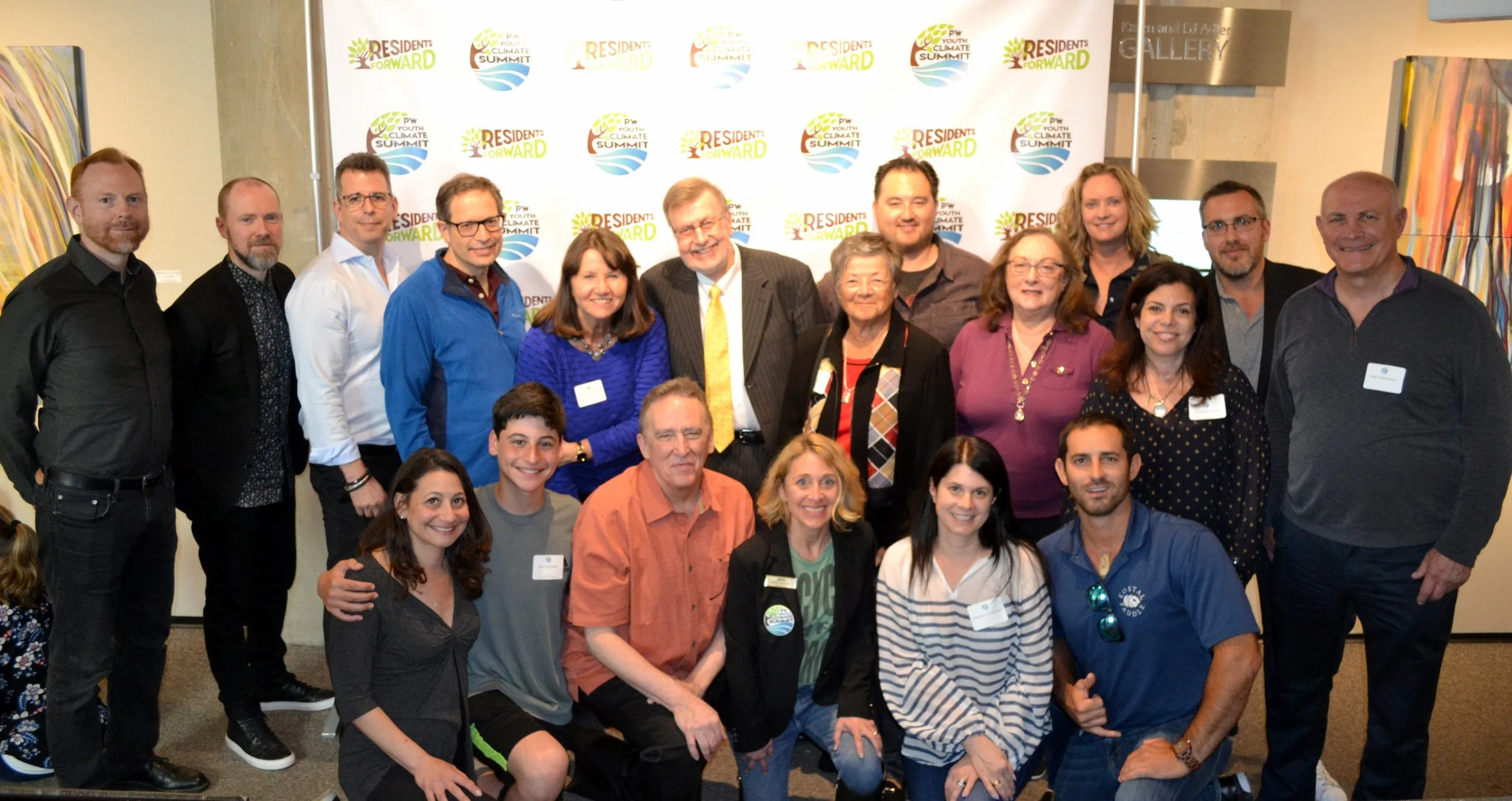 Group of 18 people posing in front of a backdrop with