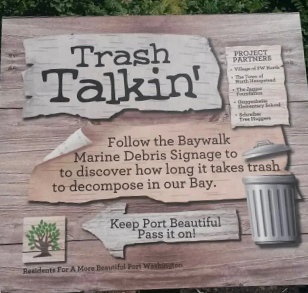 Signboard about Trash Talkin' project, encouraging people to follow the baywalk Marine Debris Signage to see how long trash takes to decompose in the bay. It lists project partners including Village of FWN, The Town of North Hueneme, The Spoon Foundation, Georganized Elementary School, and Shrubbar Tree Waggers. There is a trash can illustration on the right and a small tree logo with the text "Residents For A More Beautiful Port Washington" at the bottom left.