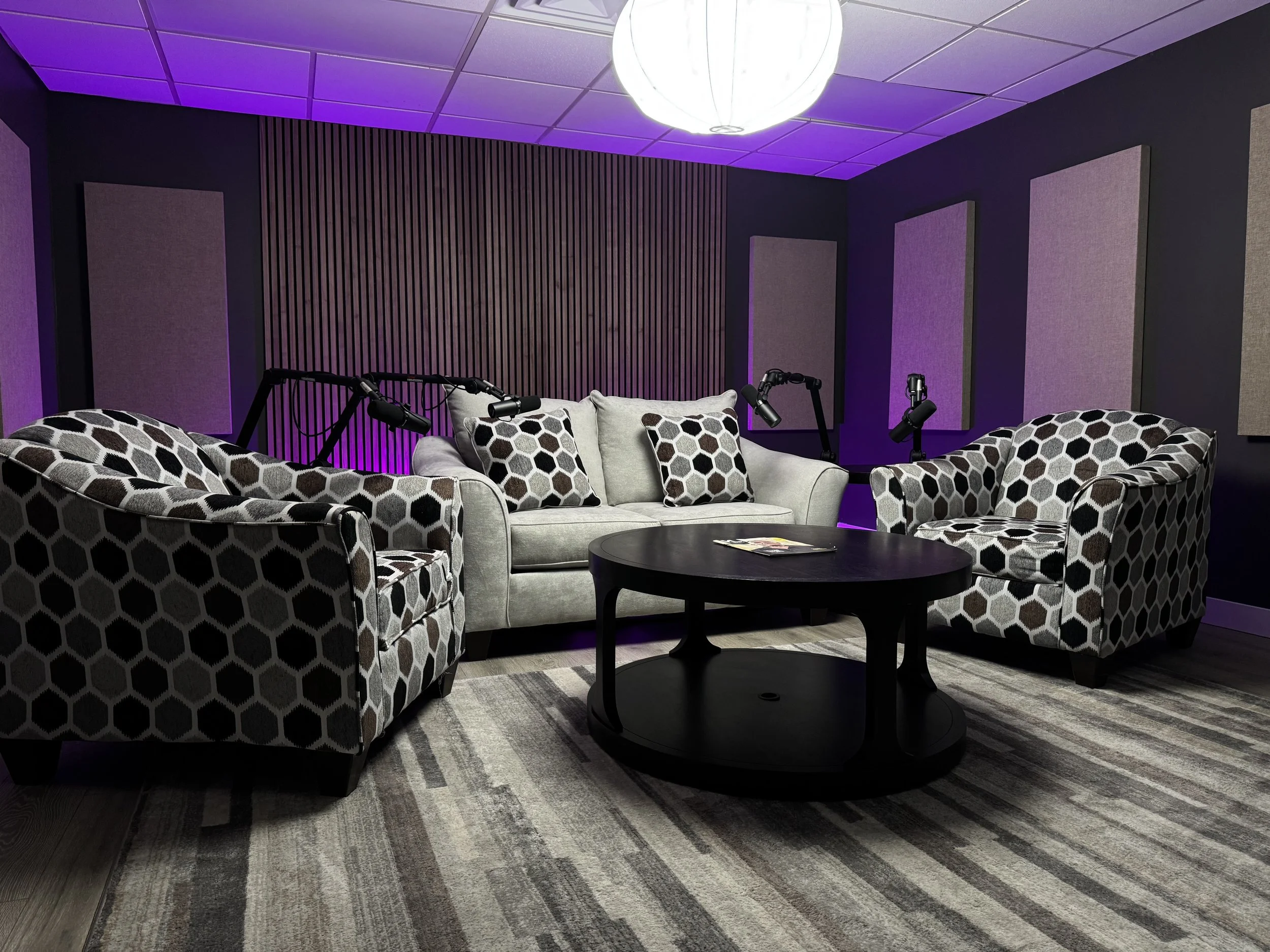 Modern podcast studio with acoustic panels, professional microphones, and lounge seating, designed for video podcast recording and content creation in a sound-treated studio environment.