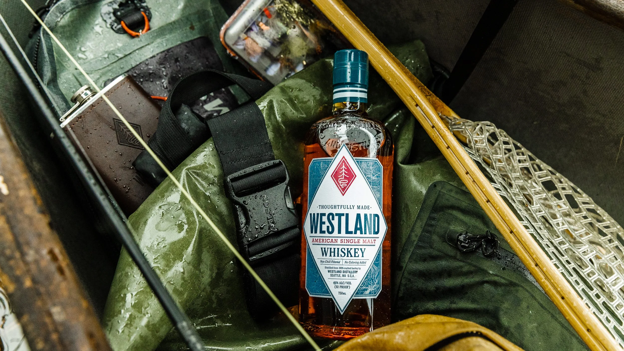 Westland American single malt whiskey bottle in outdoor fly fishing setting showcasing lifestyle branding and packaging