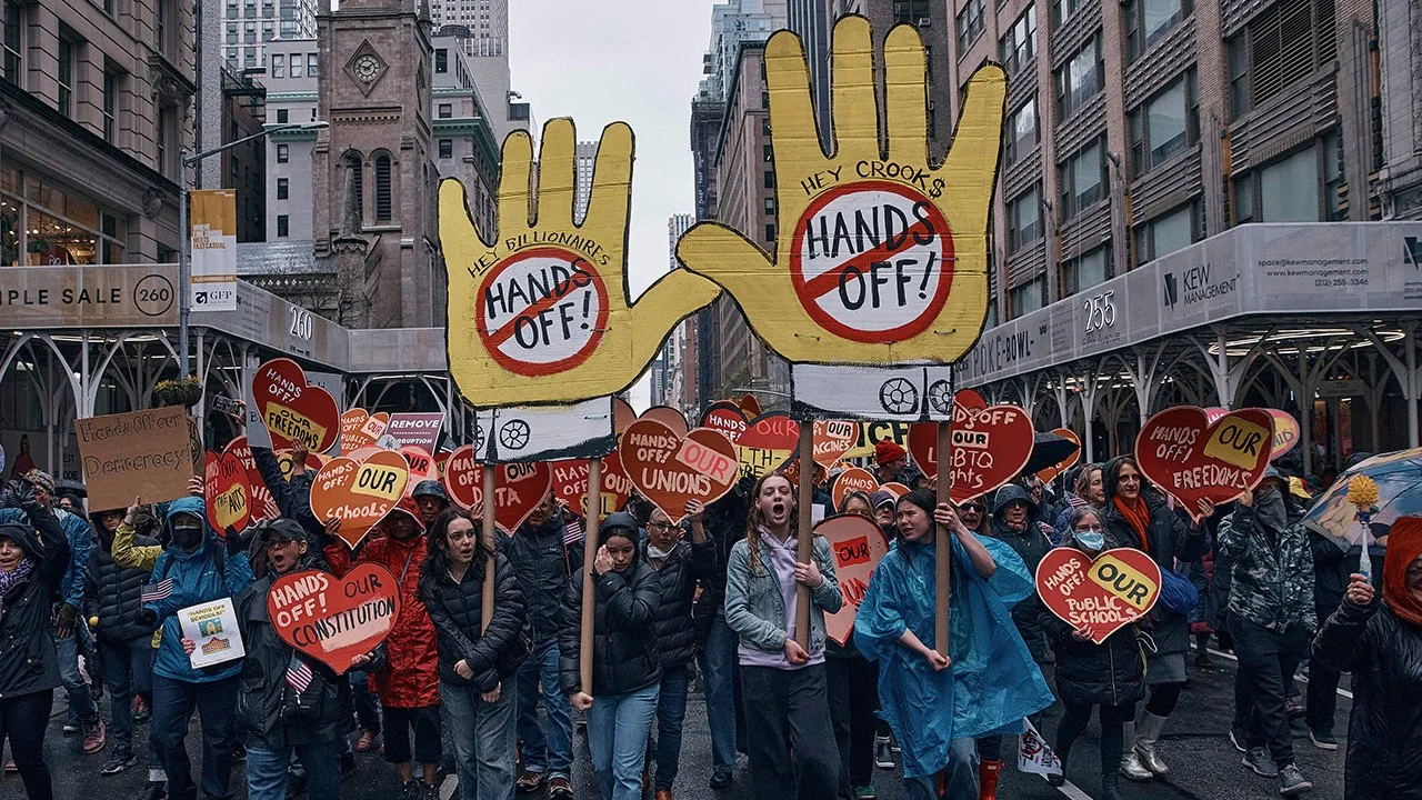 Protest marchers on a Manhattan street holding signs that say "Hands Off!"