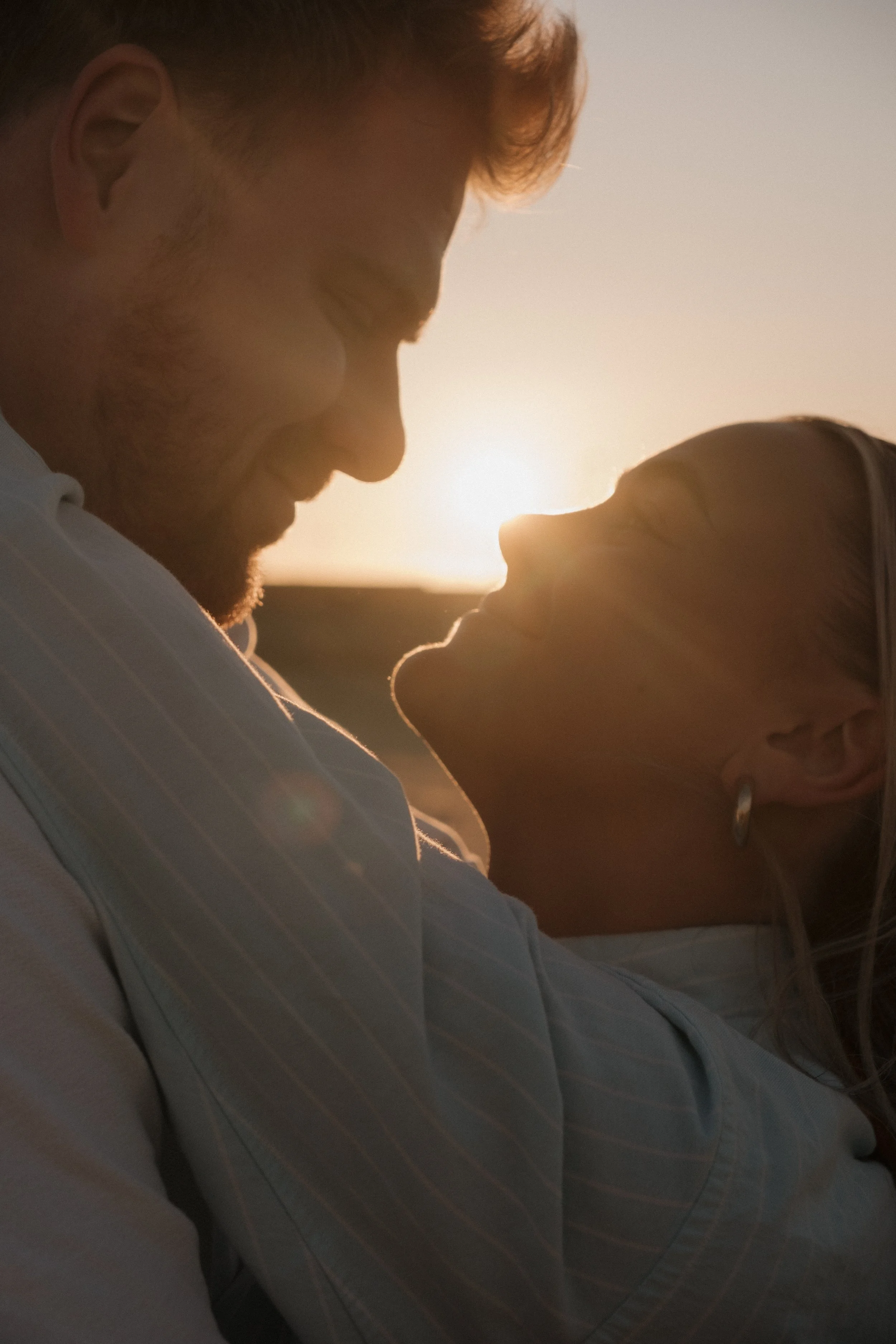 A couple facing each other closely at sunset, with the sun behind them, creating a warm glow.