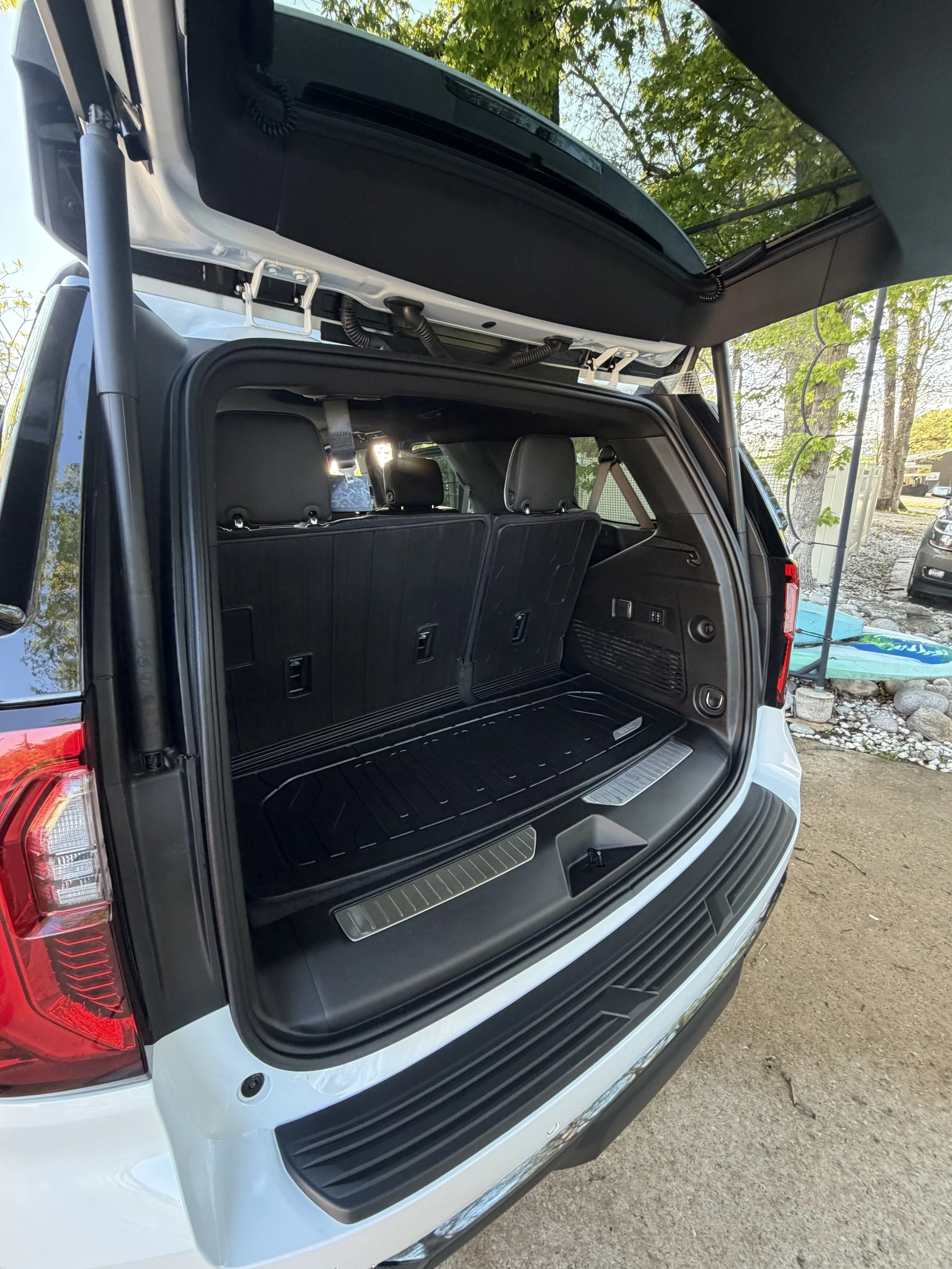 A black SUV with its rear hatch open outdoors, revealing the cargo space and rear seats, with trees and a cloudy sky in the background.