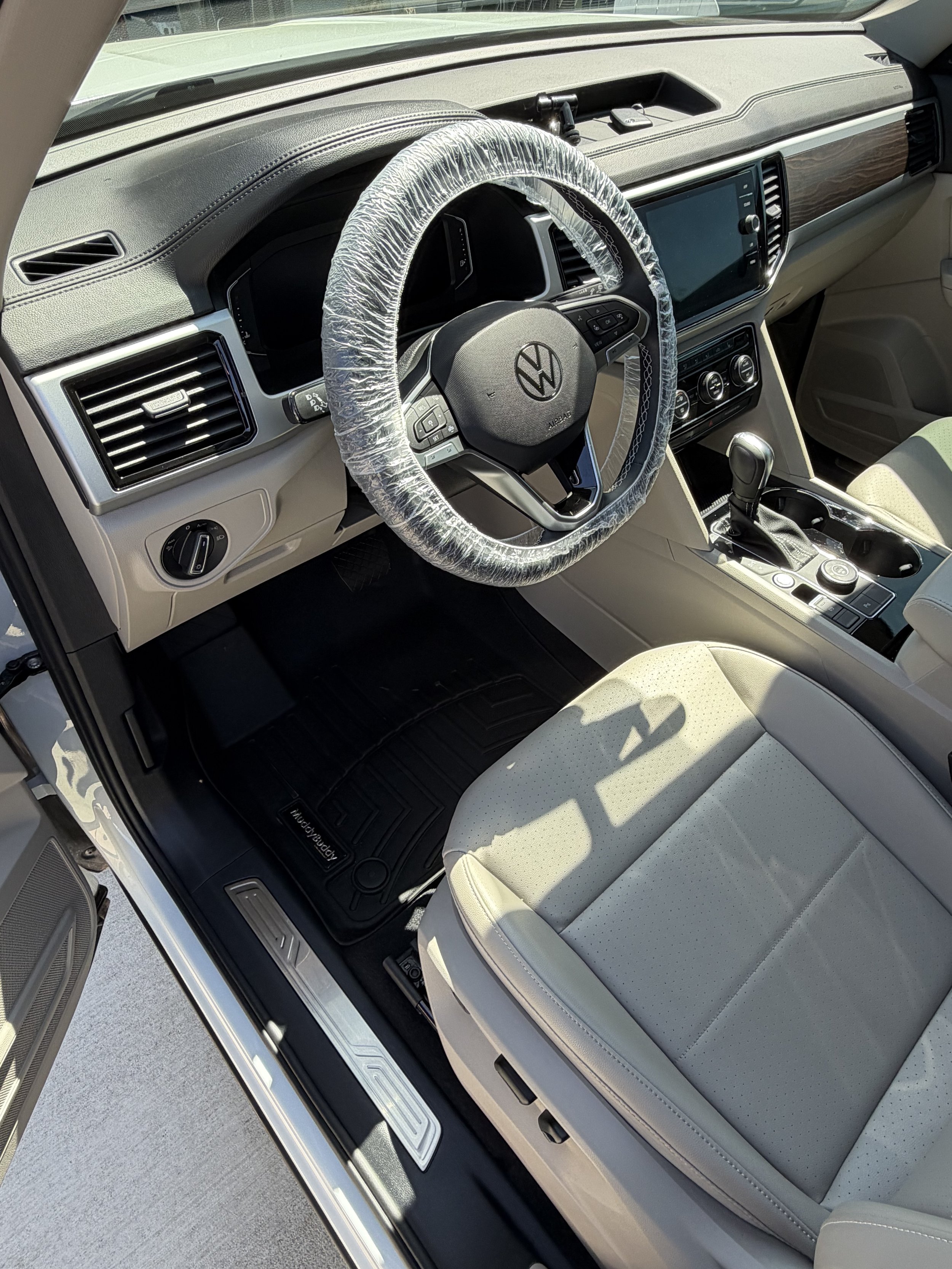 Interior of a Volkswagen vehicle showing the steering wheel with a plastic cover, dashboard, control panel, gear shift, and beige seat.