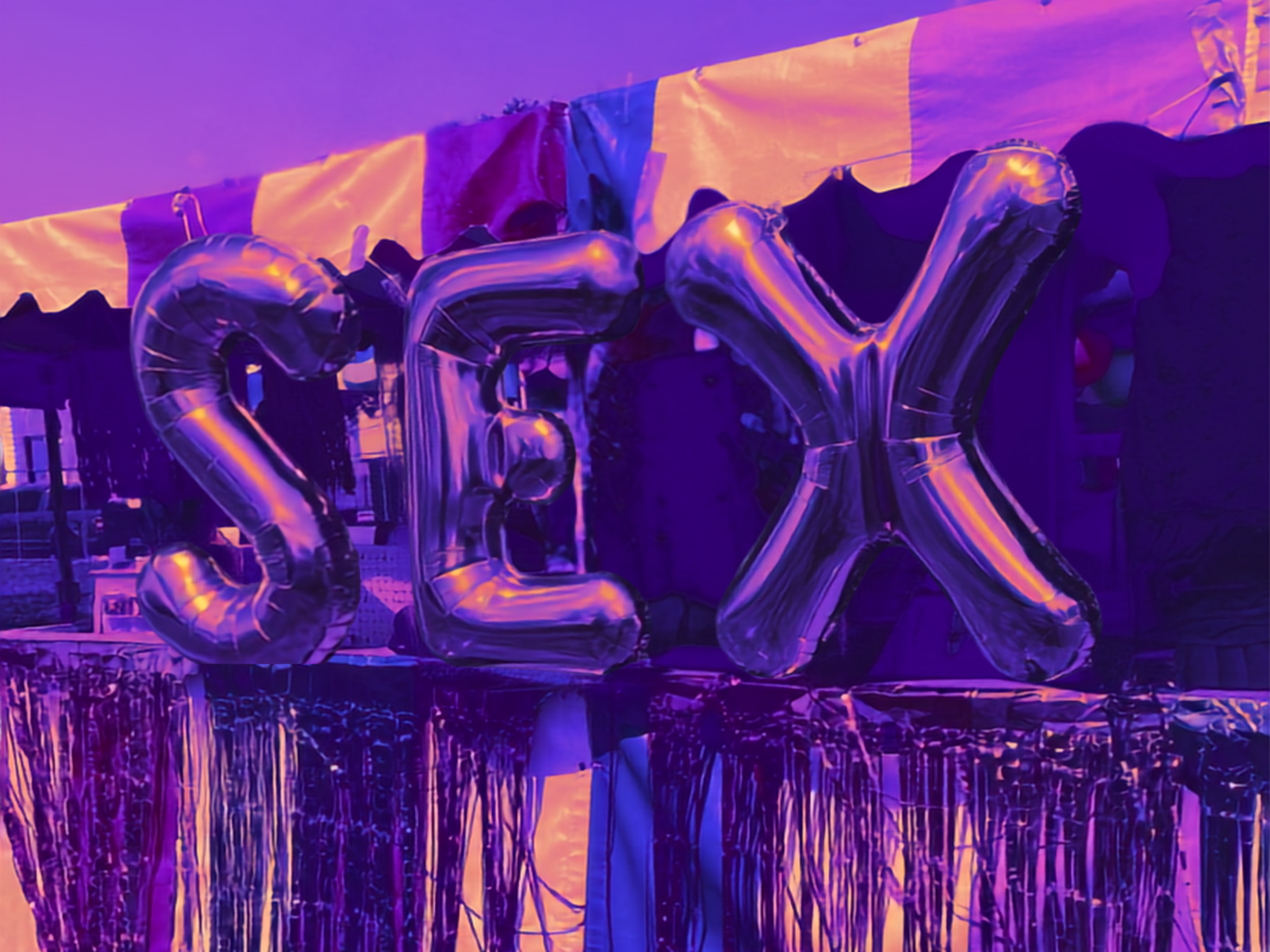 Colorful, reflective balloon art sculpture with vibrant purple, pink, and orange hues, set against a purple sky background.