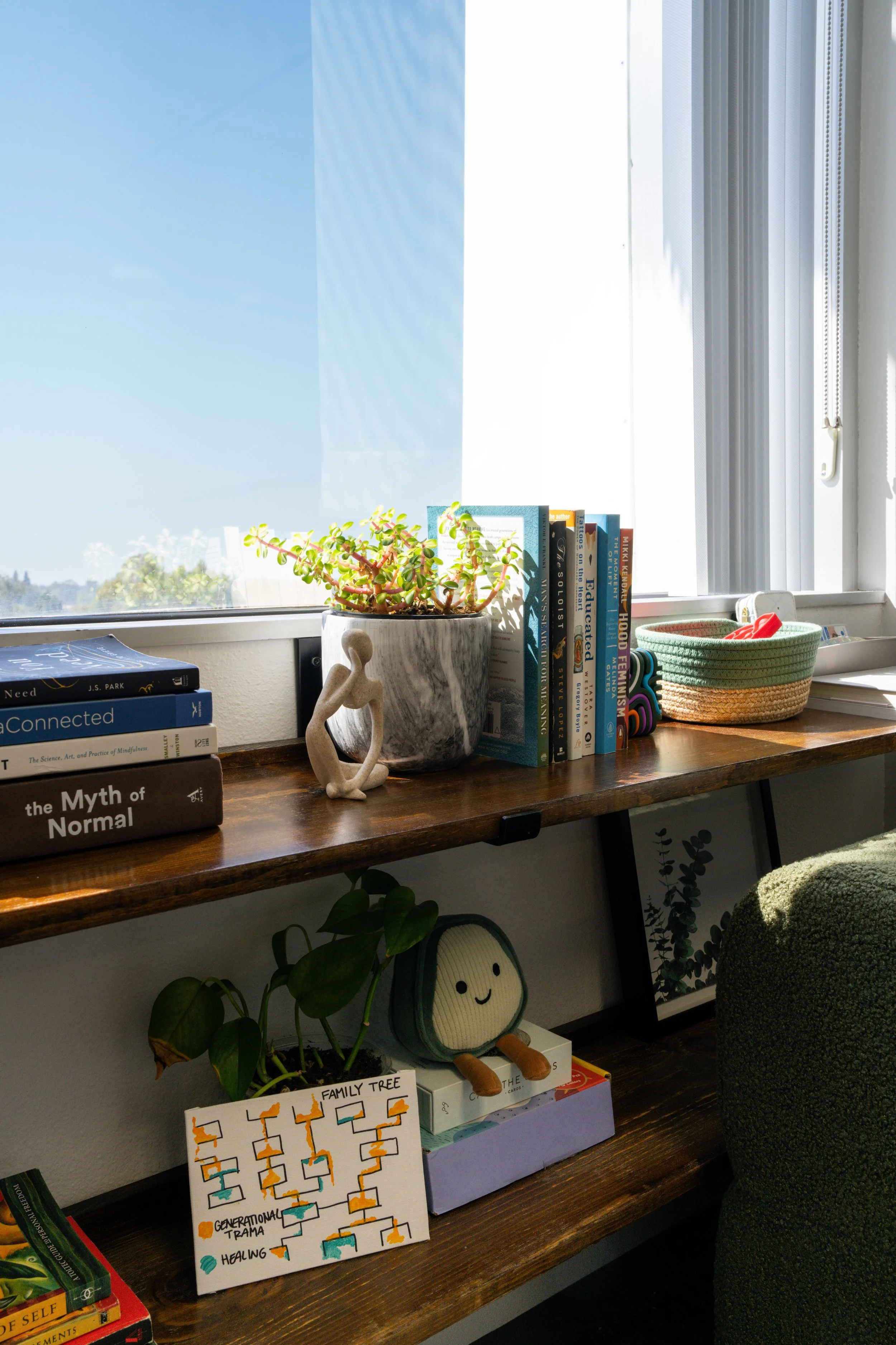 A wooden shelf by a window with books, a potted plant, and small decorative items including a sculpture and a plush toy.