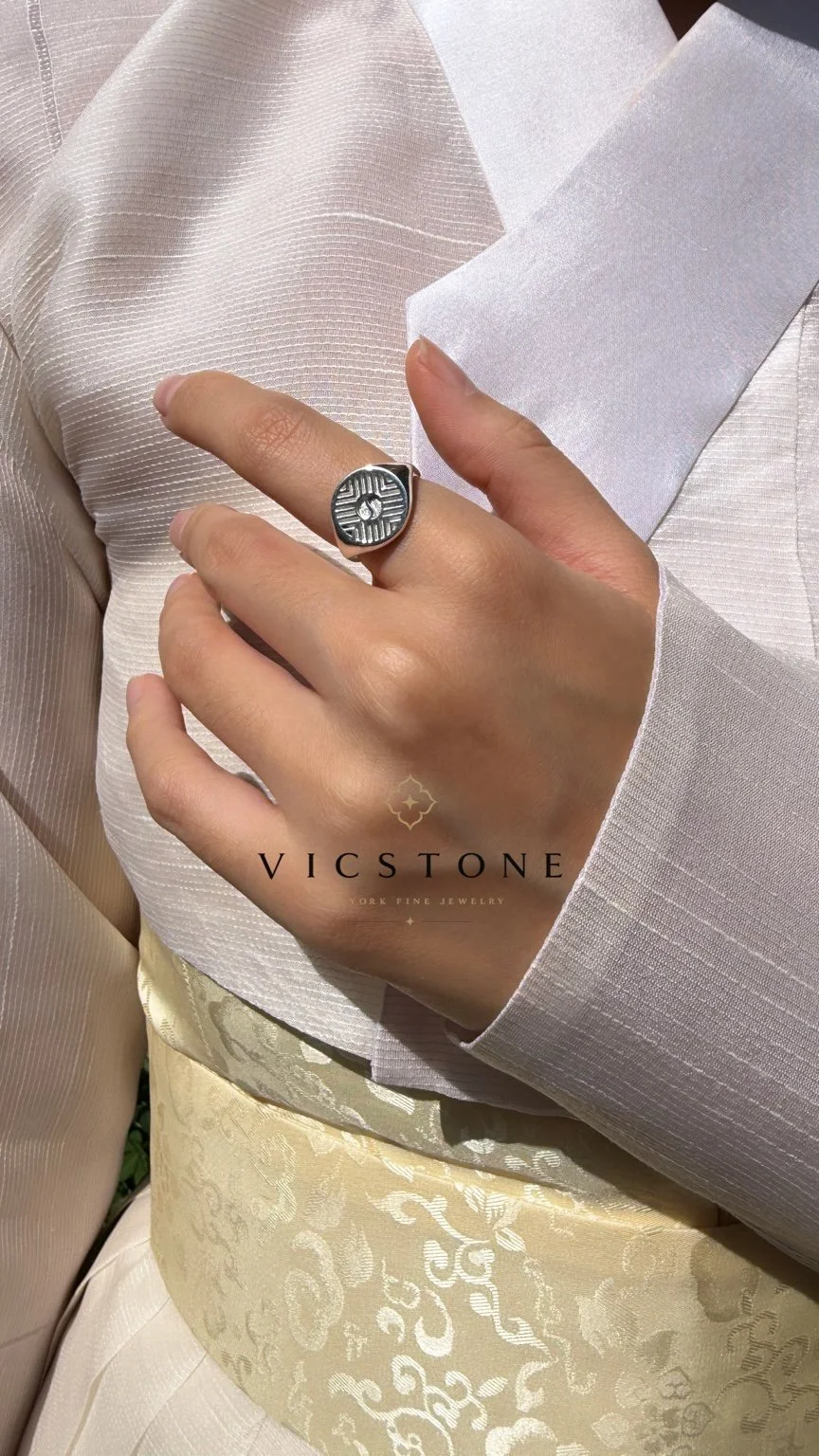 A close-up of a hand displaying a silver ring against a light-colored textured fabric and silk ribbons, with a logo reading 'VICSTONE' at the bottom. 태극 반지 광복절 뉴욕에서 한국 무용수 님과