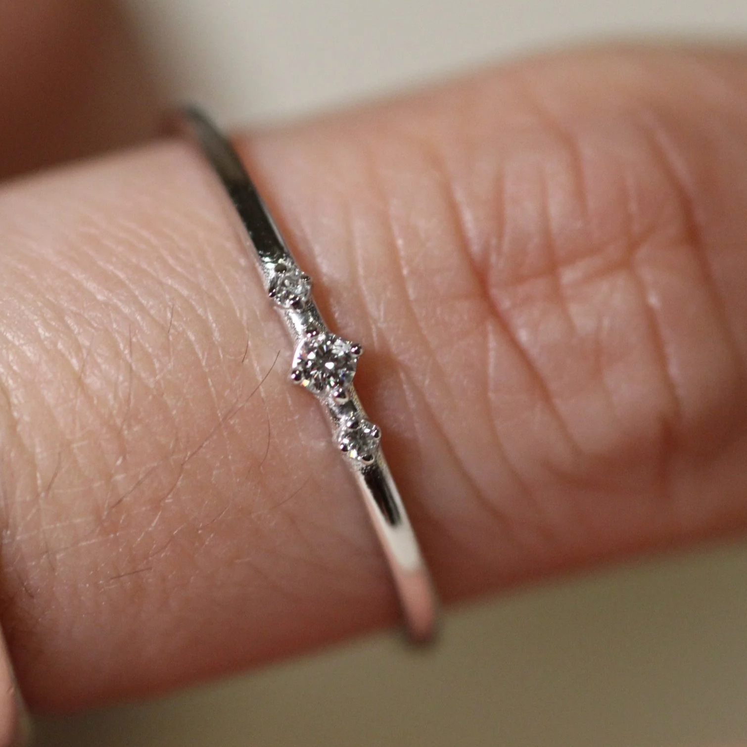 Dainty 14K gold diamond stacking ring with three clear stones, worn on finger, minimalist fine jewelry, perfect for gift or everyday styling