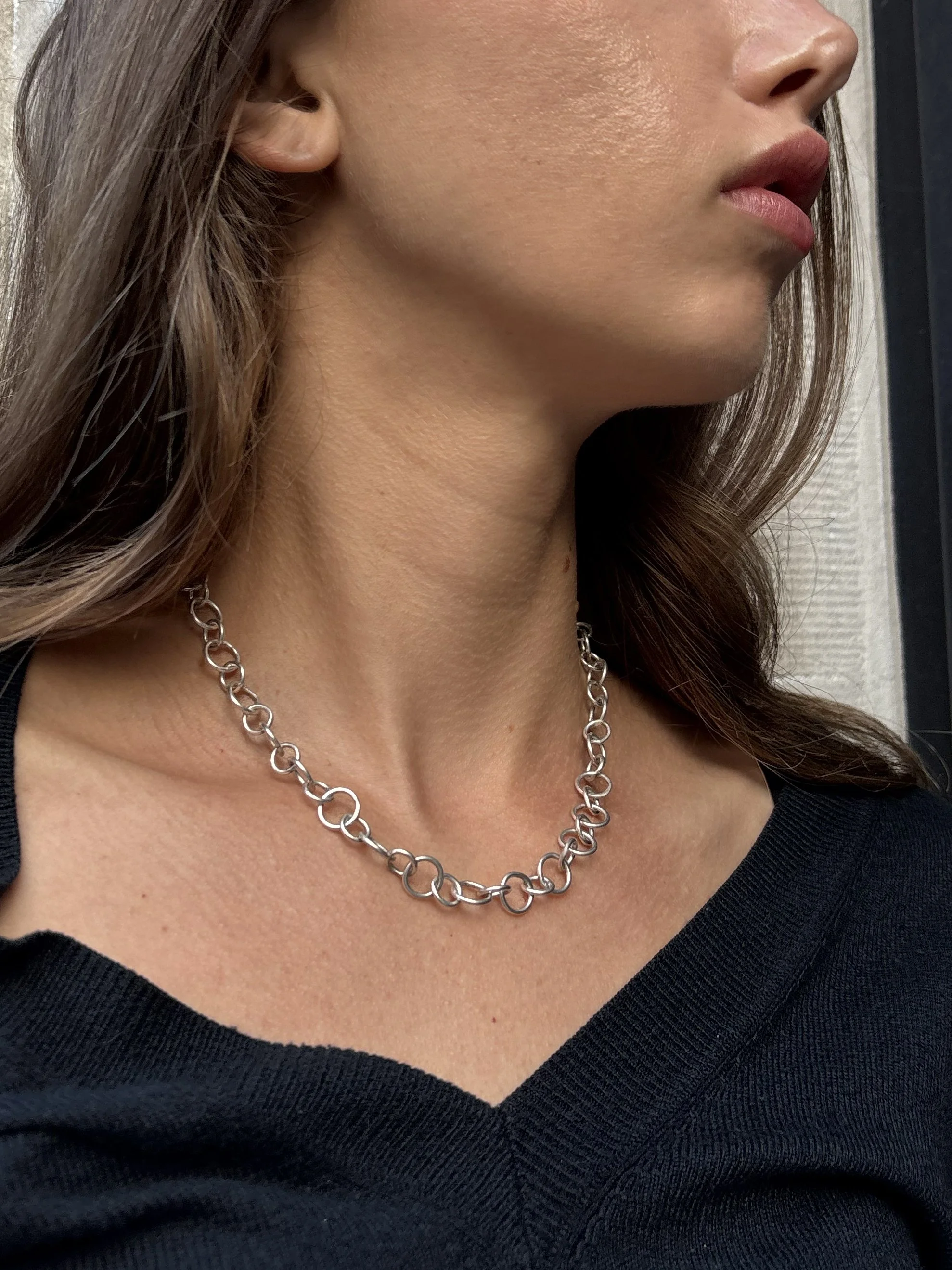 Close-up of a woman wearing a silver chain necklace and a black top, with part of her face visible including her lips and nose.