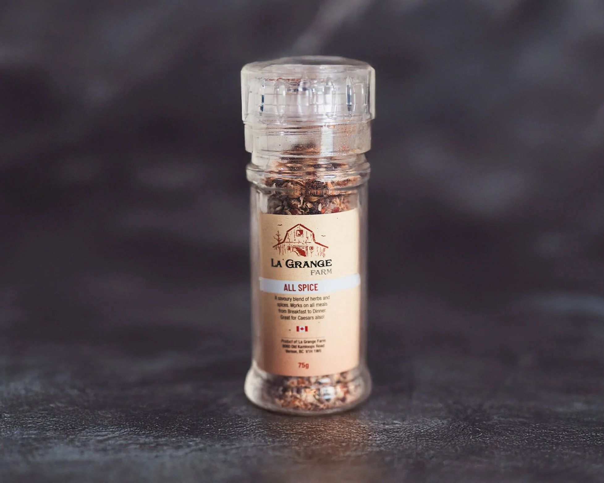 Clear spice grinder labeled 'La Grange Farm All Spice' on dark background.