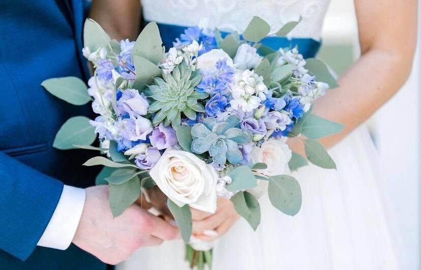 Bride and groom holding a bouquet with blue, purple, and white flowers, including succulents and eucalyptus leaves.