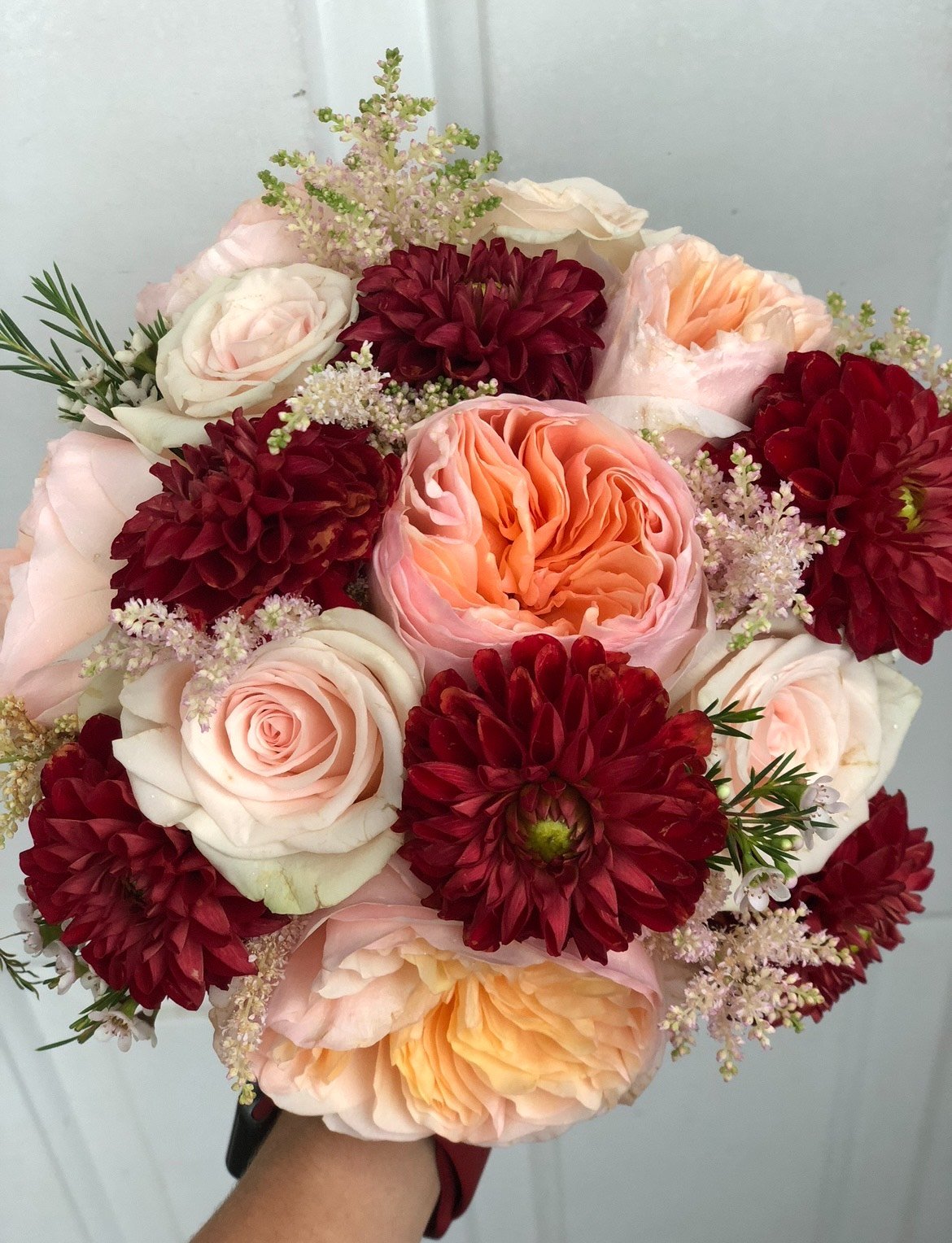Bouquet of red dahlias, pink and peach roses, and light pink astilbe flowers.
