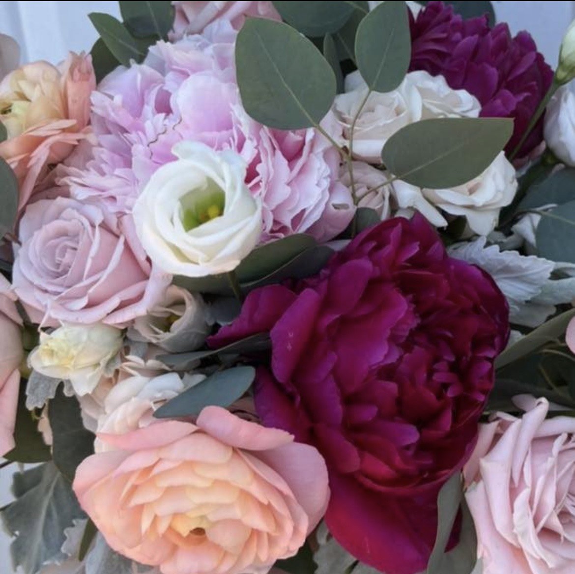 Close-up of a bouquet featuring assorted flowers in shades of pink, white, and deep red, with leafy greenery.