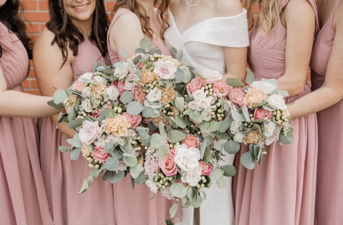 Bridesmaids in mauve dresses holding bouquets of flowers including roses and eucalyptus leaves.
