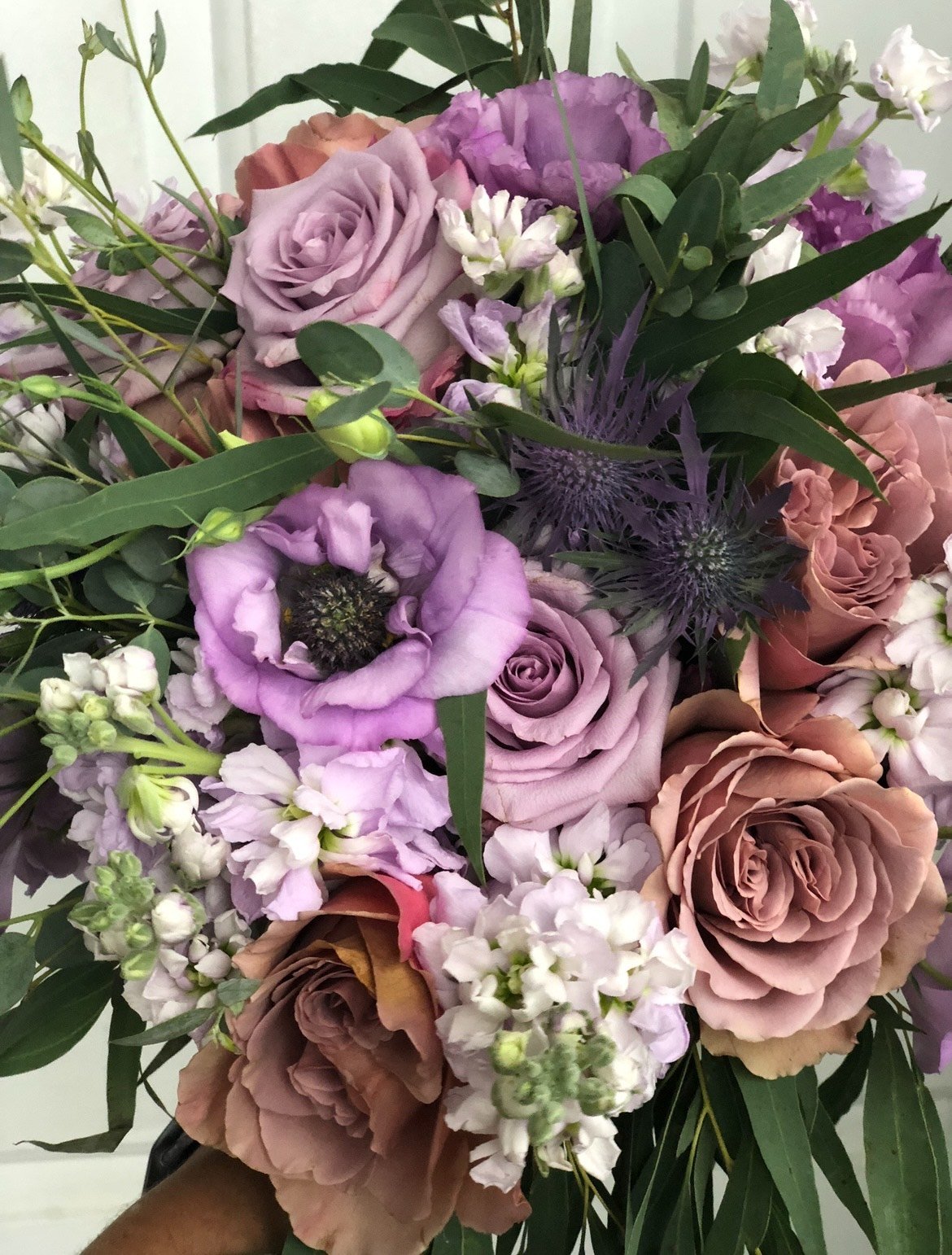 Bouquet of purple and pink flowers including roses and lisianthus with green leaves