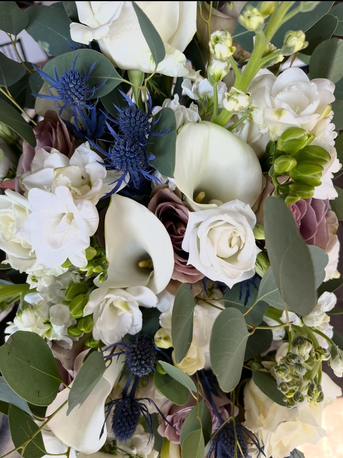Bouquet with white calla lilies, roses, blue thistles, eucalyptus leaves, and other flowers.