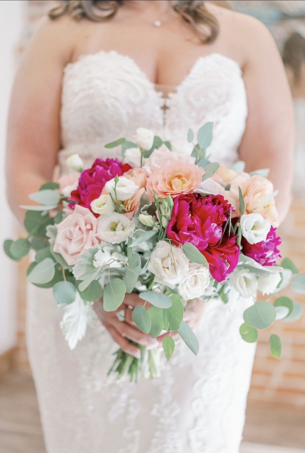 Bride holding a vibrant floral bouquet with pink, white, and red flowers, including roses and eucalyptus leaves.
