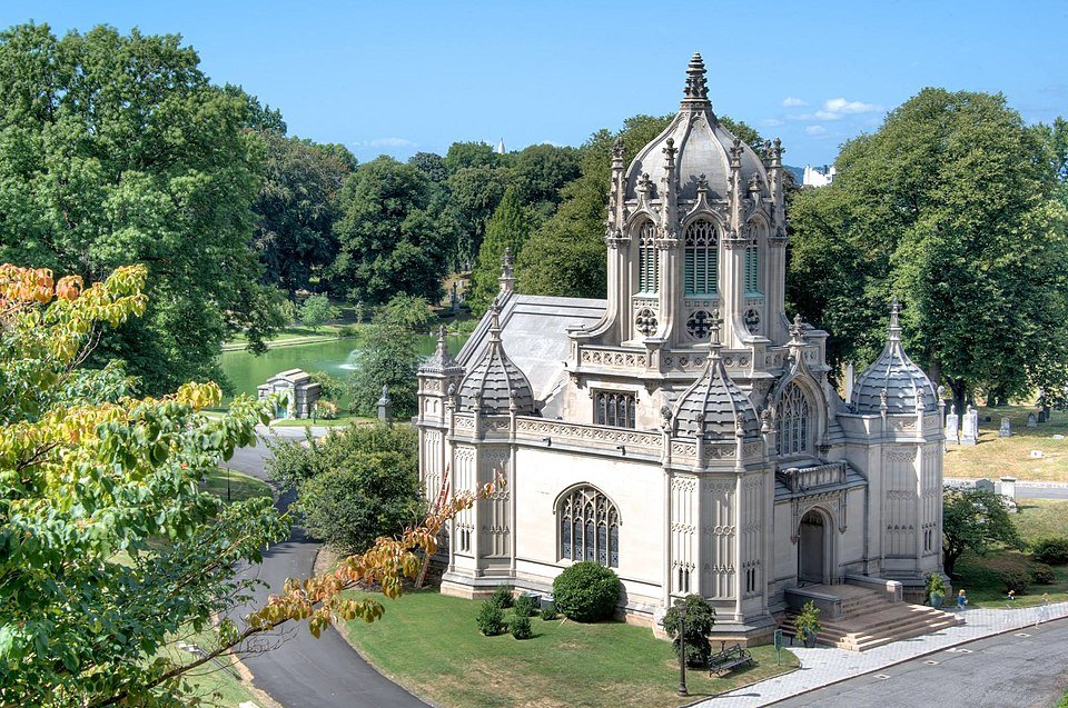 A white Gothic-style chapel with intricate architectural details, surrounded by lush green trees and a well-maintained lawn.